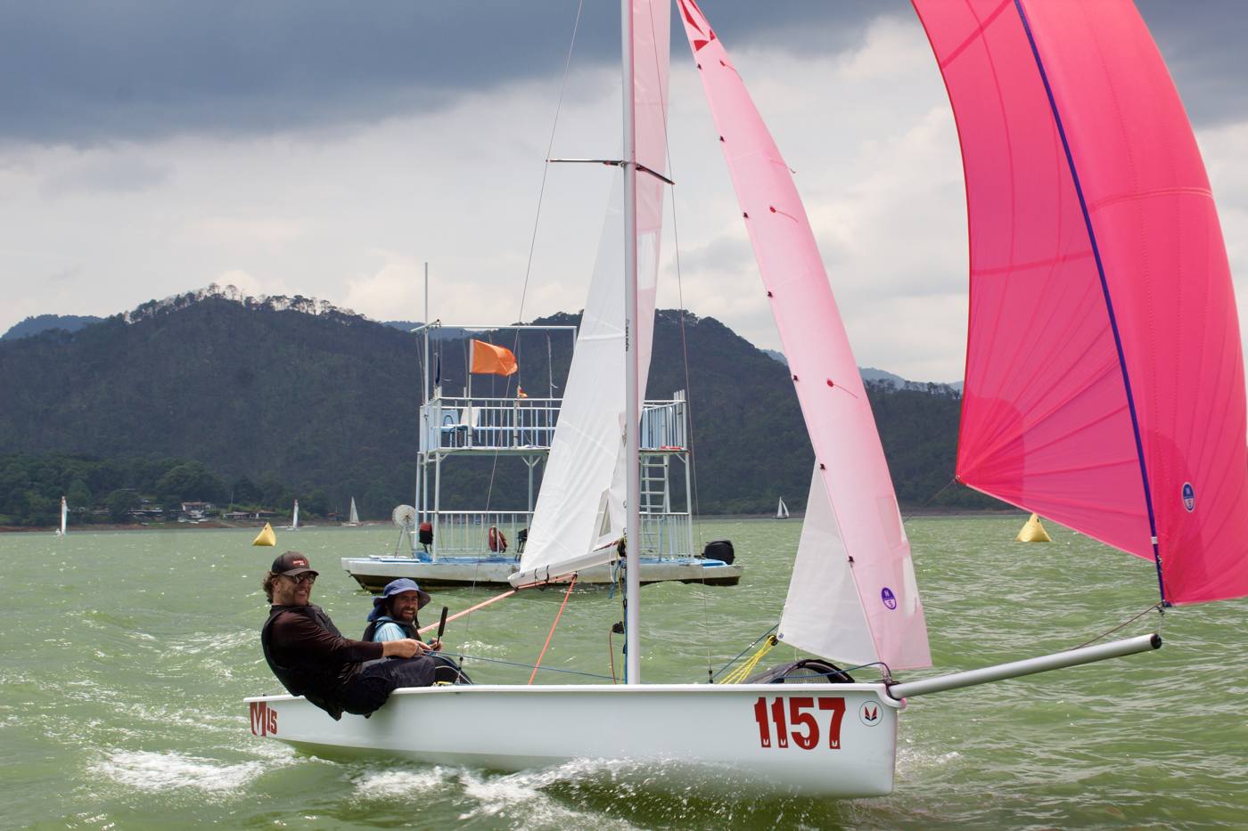 Dos amigos sonriendo a bordo de un Melges 15 con spinnaker rosa